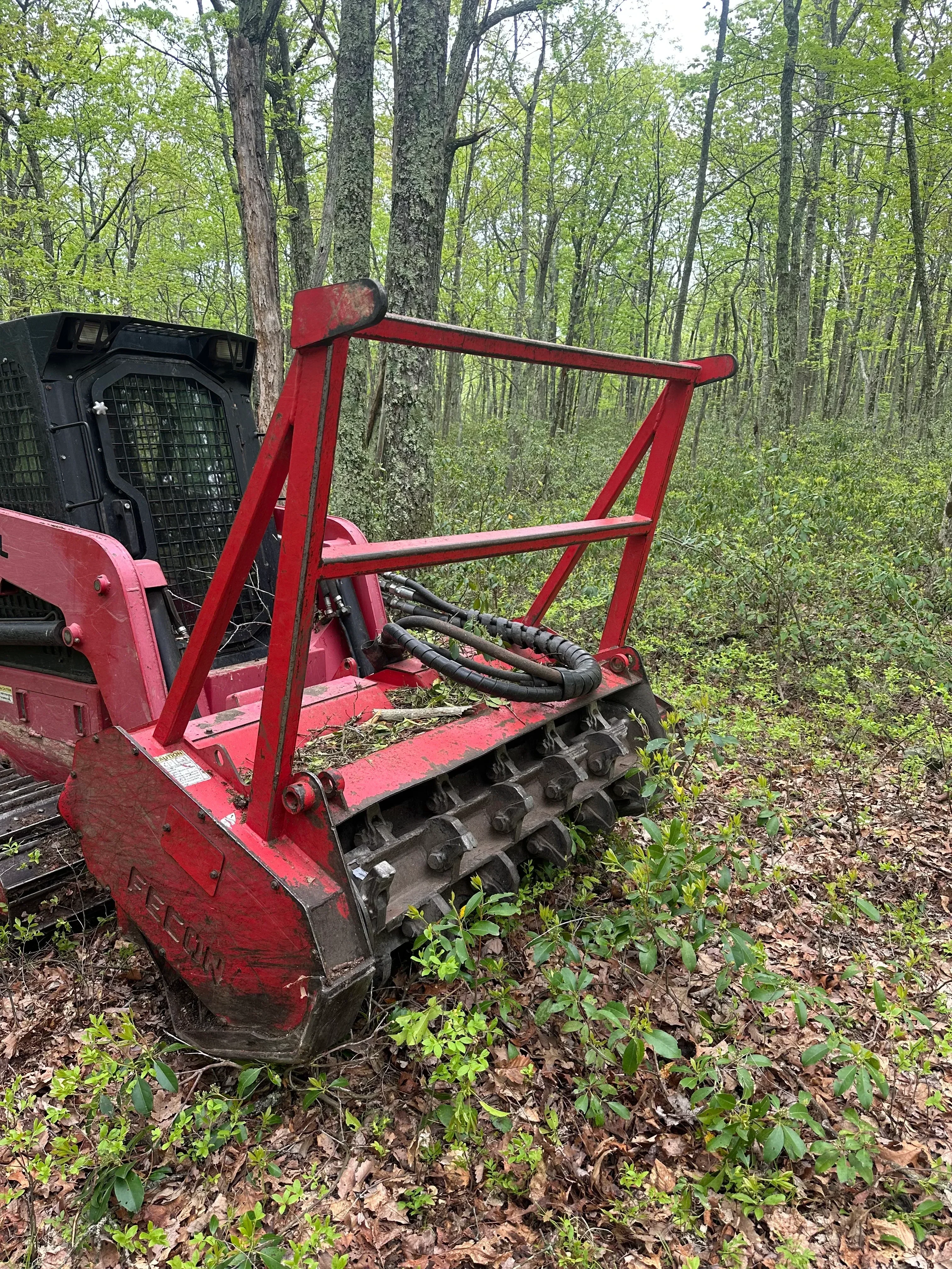 Red wood chipper with hydraulic feed system processing tree limbs and vegetation on cleared property