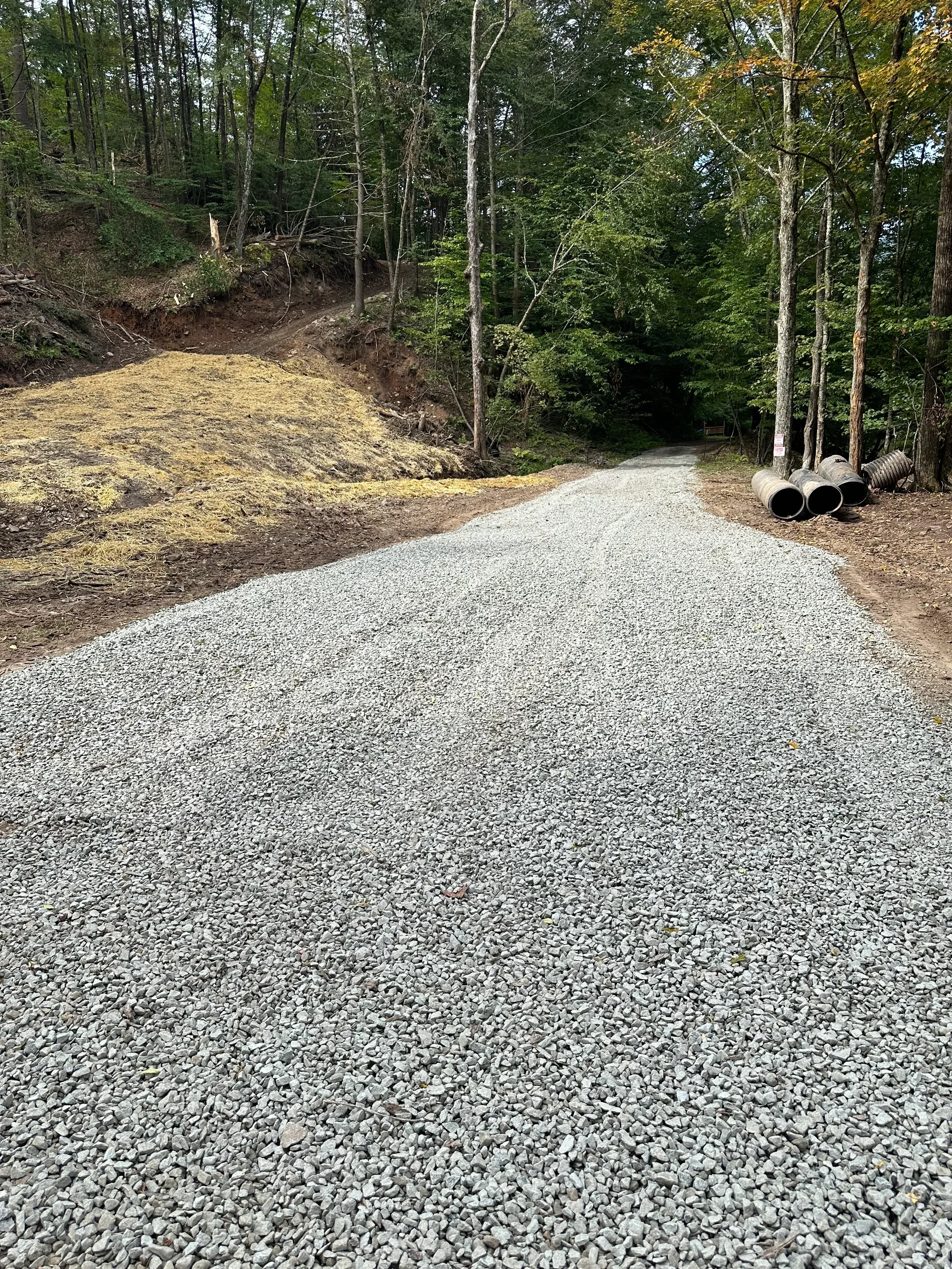 Gravel driveway with metal drainage pipes and cleared vegetation along edges