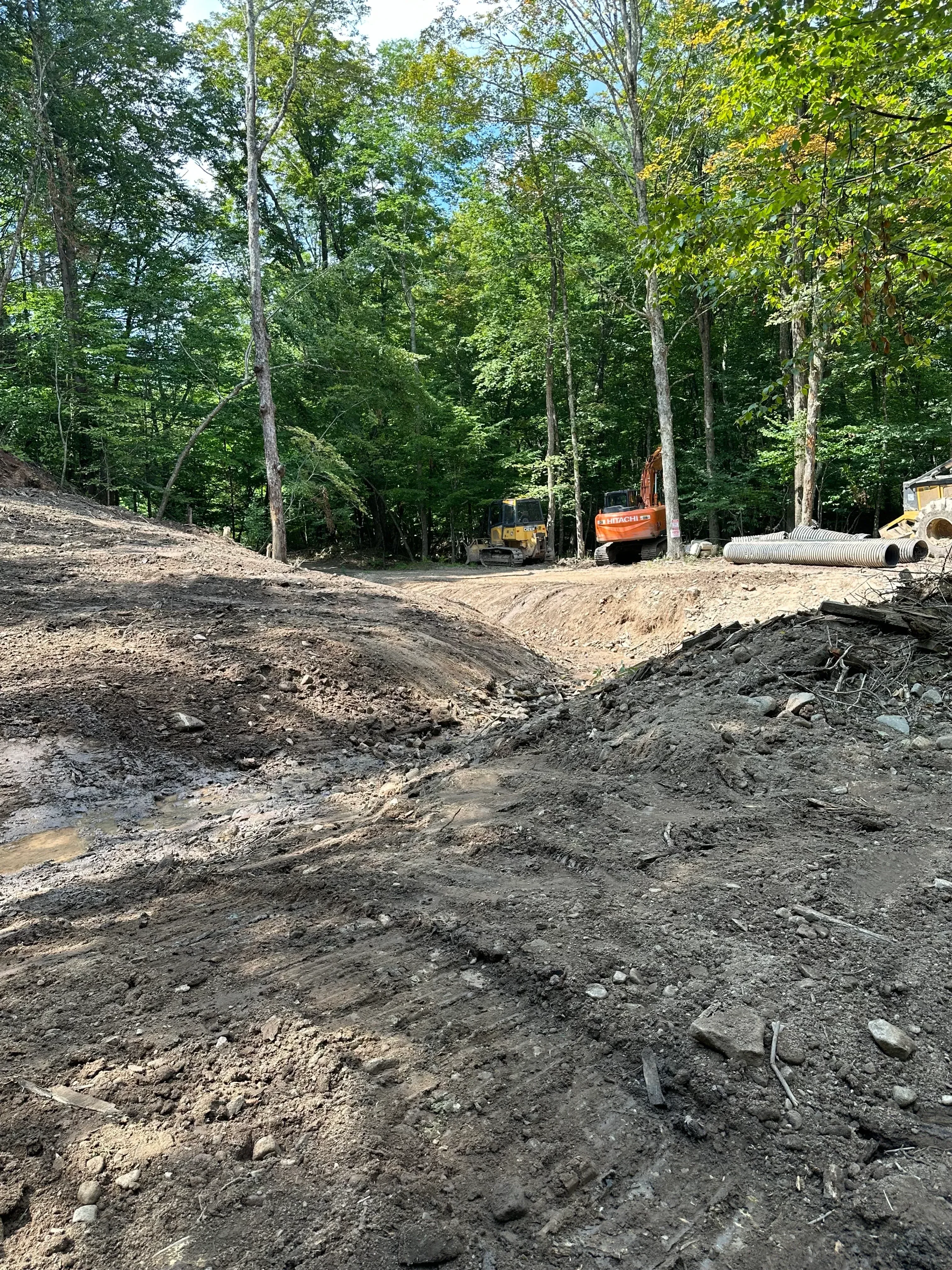 Excavated driveway with graded earth, heavy equipment, and surrounding trees