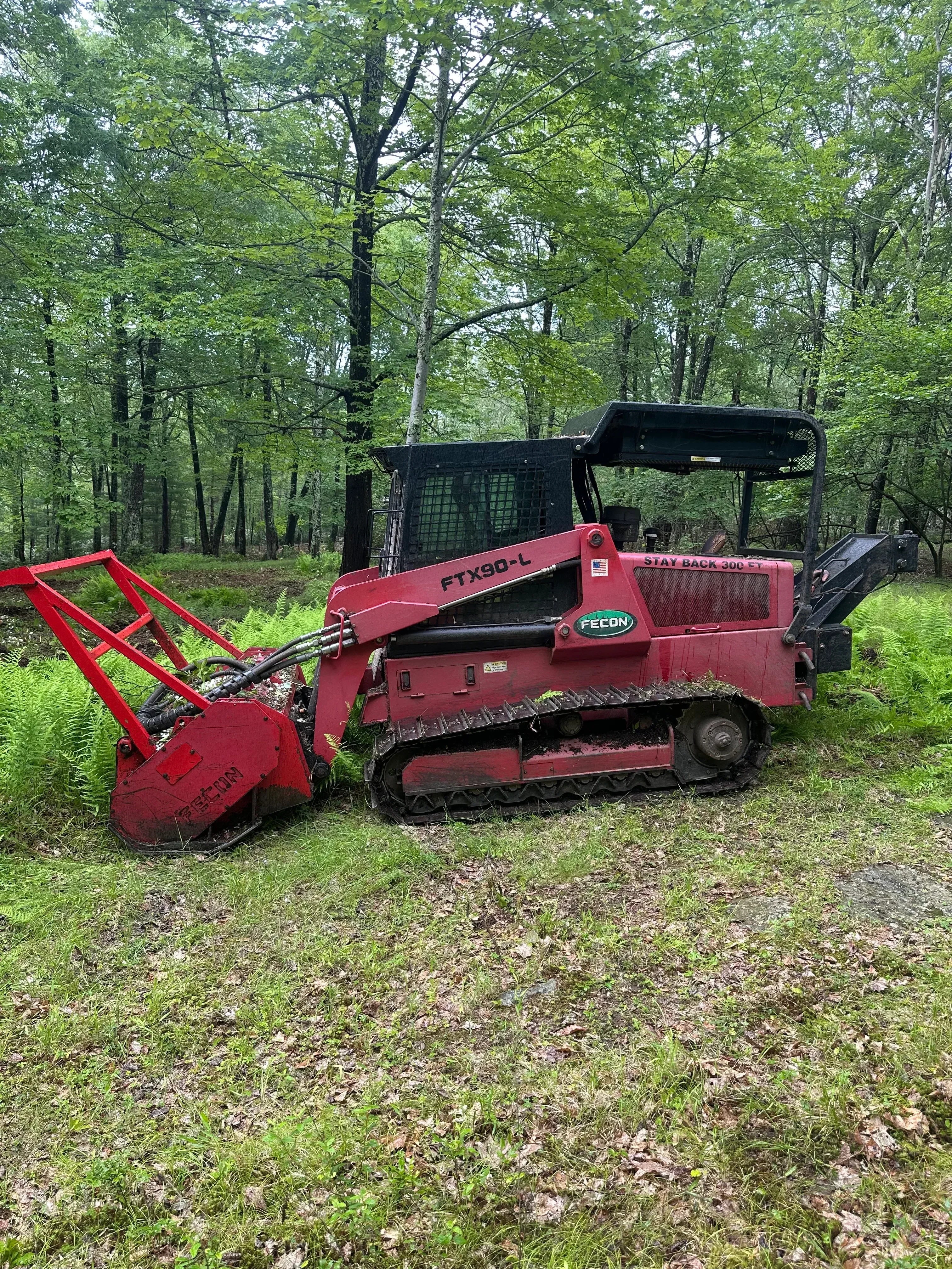 Red Fecon forestry mulcher on tracked carrier in wooded area with vegetation