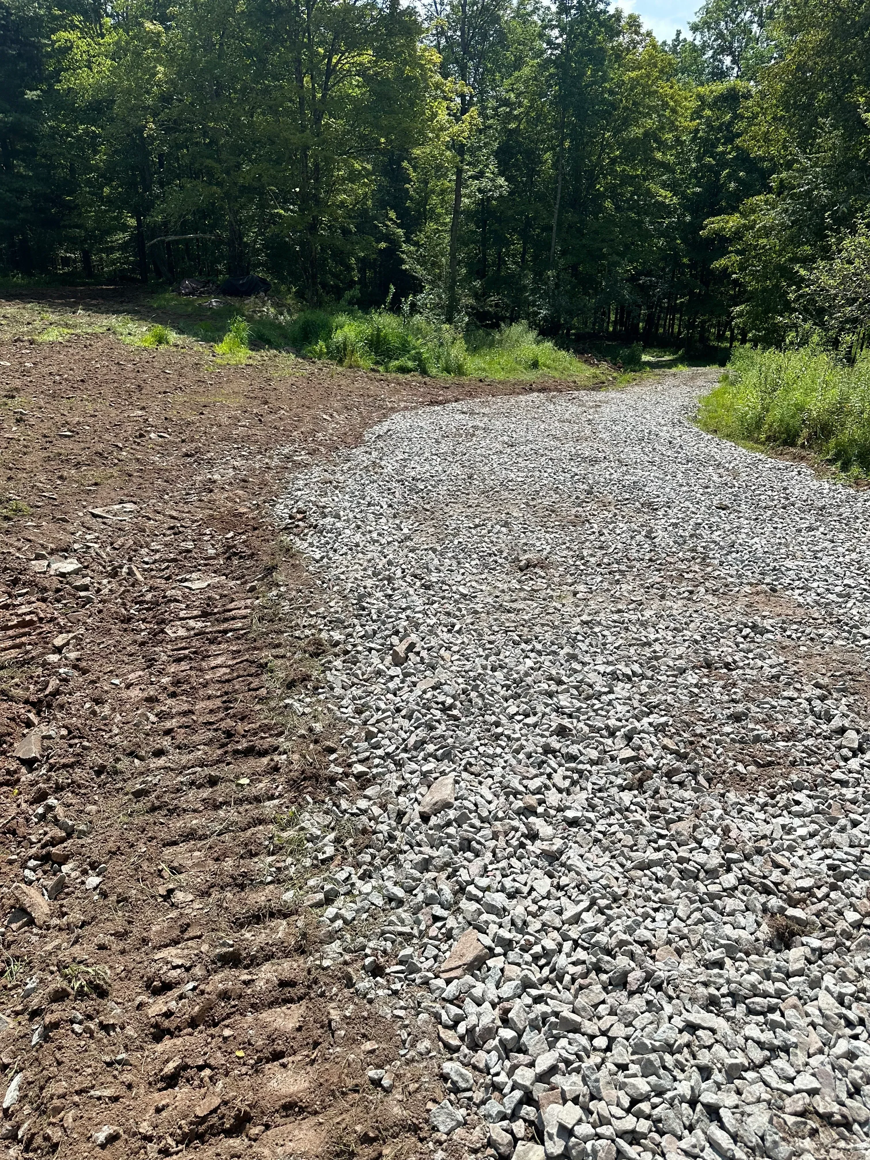 Crushed gravel and stone road base material freshly installed on cleared land with green vegetation border
